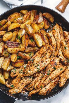 chicken and potatoes in a skillet on a white table with a wooden spatula