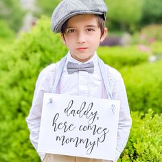 a young boy is holding a sign that says daddy here comes mommy on his chest