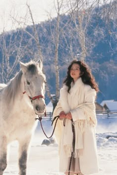 a woman standing next to a white horse in the snow