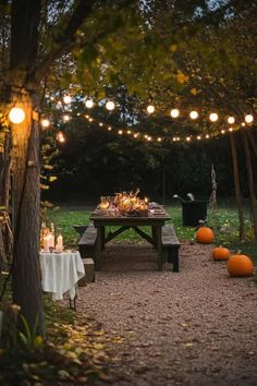 an outdoor dining area with lights strung over the table and pumpkins on the ground