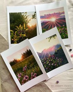 four cards with pictures of mountains and flowers in them on a piece of cloth next to buttons