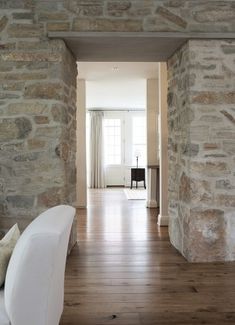 the hallway is lined with stone walls and wood flooring, along with a white couch