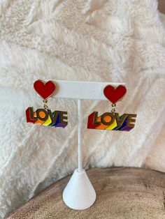 the earrings are on display in front of a white furnishing background with red, yellow, and blue hearts