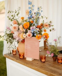 an arrangement of flowers in vases on a wooden table with candles and menu card