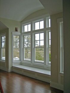 an empty room with three large windows and hard wood flooring