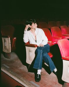 a woman sitting in an empty theater seat with her hand on her head and looking off to the side