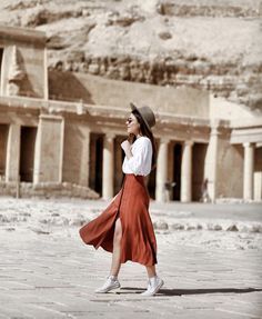 a woman wearing a hat and dress walking in front of an ancient building with columns