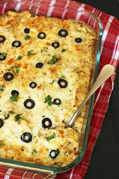 a casserole with olives and cheese in a glass dish on a red checkered cloth