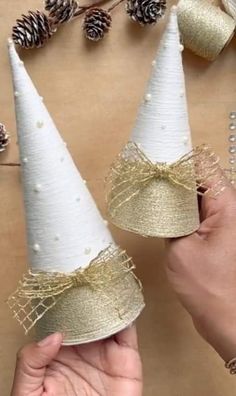 two white cones with gold ribbon and pine cones on the top are being held by someone's hand