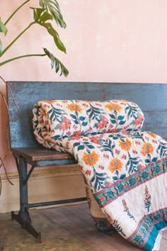 a wooden bench with a quilt on it next to a potted plant