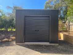 a metal garage with an open door in the middle of a gravel area next to rocks and trees