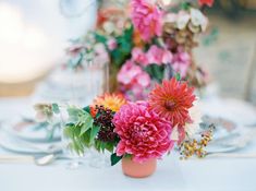 colorful flowers are in a vase on a white table cloth with silverware and wine glasses