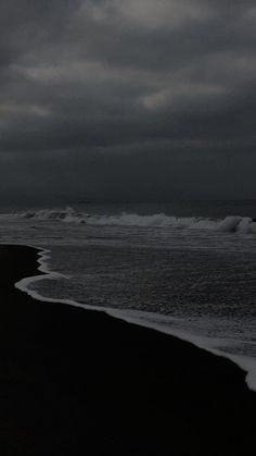 an empty beach with waves coming in to the shore and dark clouds above it on a gloomy day