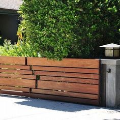 a wooden fence with a lantern on top in front of some bushes and trees,