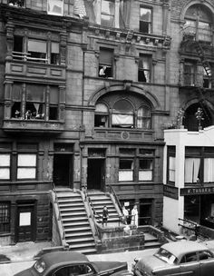 an old black and white photo of cars parked in front of a building with stairs