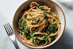 a bowl filled with noodles and spinach on top of a white table next to a fork