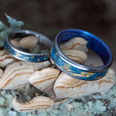 two wedding rings sitting on top of some sea shells next to each other with blue and gold paint