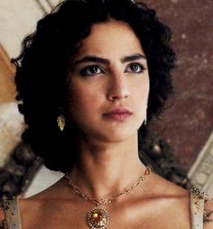 a woman in a white dress wearing a gold necklace and earring with an ornate design on it