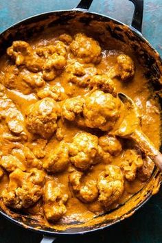 a skillet filled with meatballs and gravy on top of a blue table