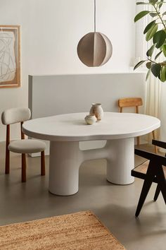 a white table with two chairs and a plant in the corner next to it on top of a rug