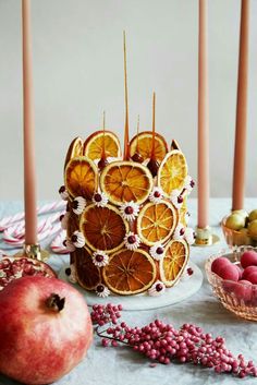 a cake with orange slices on it sitting next to some fruit and two candles in the background