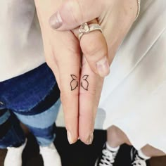 a woman's hand with a small bow tattoo on the middle finger and two fingers