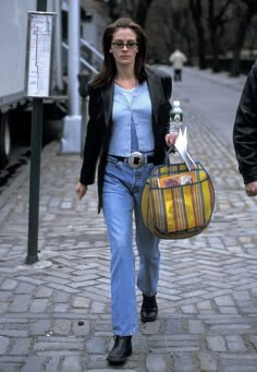 a woman walking down the street carrying a bag and a bottle in her hand,