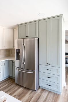 a stainless steel refrigerator in a kitchen with white cabinets and wood flooring on the walls