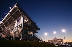 an empty stadium stands at night with people standing around and watching the lights shine on it