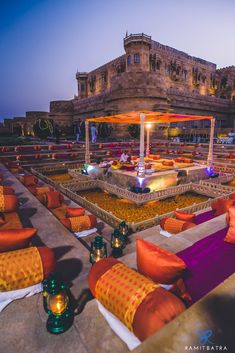 an outdoor seating area in front of a building at night with colorful lights on it