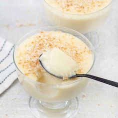 two glasses filled with ice cream on top of a white tablecloth and silver spoon