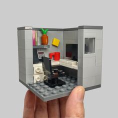 someone is holding up a lego model of a small kitchen and dining area in their hand