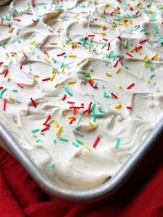 a pan filled with white frosting and sprinkles on top of a red cloth