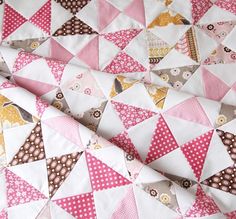 a close up of a pink and white quilt with many different colored triangles on it