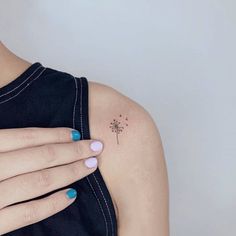 a woman's hand with a small tattoo on her left shoulder, and a dandelion in the middle