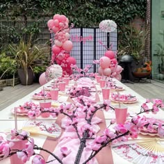 a table set up with pink flowers and paper fans for an outdoor birthday party or baby shower