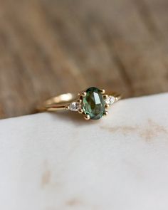 a green and white diamond ring on top of a piece of paper with wood in the background