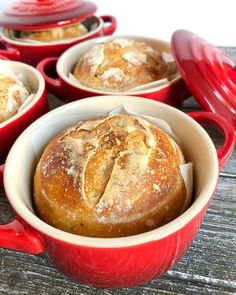 baked bread in a red pot on a wooden table next to other baking dishes and utensils