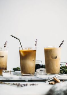 three glasses filled with iced coffee sitting on top of a white table next to flowers