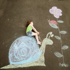 a child is sitting on top of a snail drawn in chalk with flowers and leaves