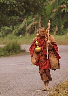 a man walking down the road with a stick and two bells on his back,