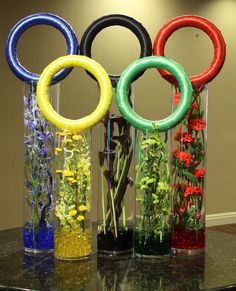 three vases with flowers in them sitting on a table next to the olympic rings