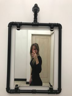 a woman taking a selfie in front of a mirror with black pipes on it