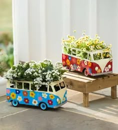 two flower pots with flowers in them sitting next to a miniature vw camper