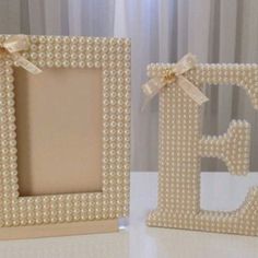 two frames with pearls and bows are sitting on a table next to each other, one has the letter b