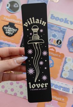 a person holding up a black bookmark with the words villain lover on it and stars