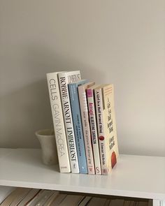 a white shelf topped with books next to a bowl