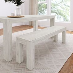 a white table with a bench in front of it on a rug next to a window