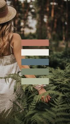 a woman in a white dress and straw hat walking through the woods with fern leaves