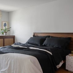 a bed with black sheets and pillows in a bedroom next to a window, near a dresser